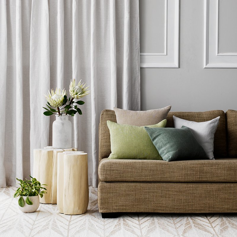 Cream textured curtains beside a beige sofa with green and blue cushions in a bright living room.