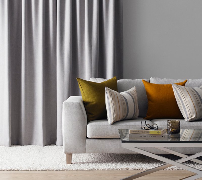 Grey textured curtains beside a cream sofa with mustard and orange cushions.