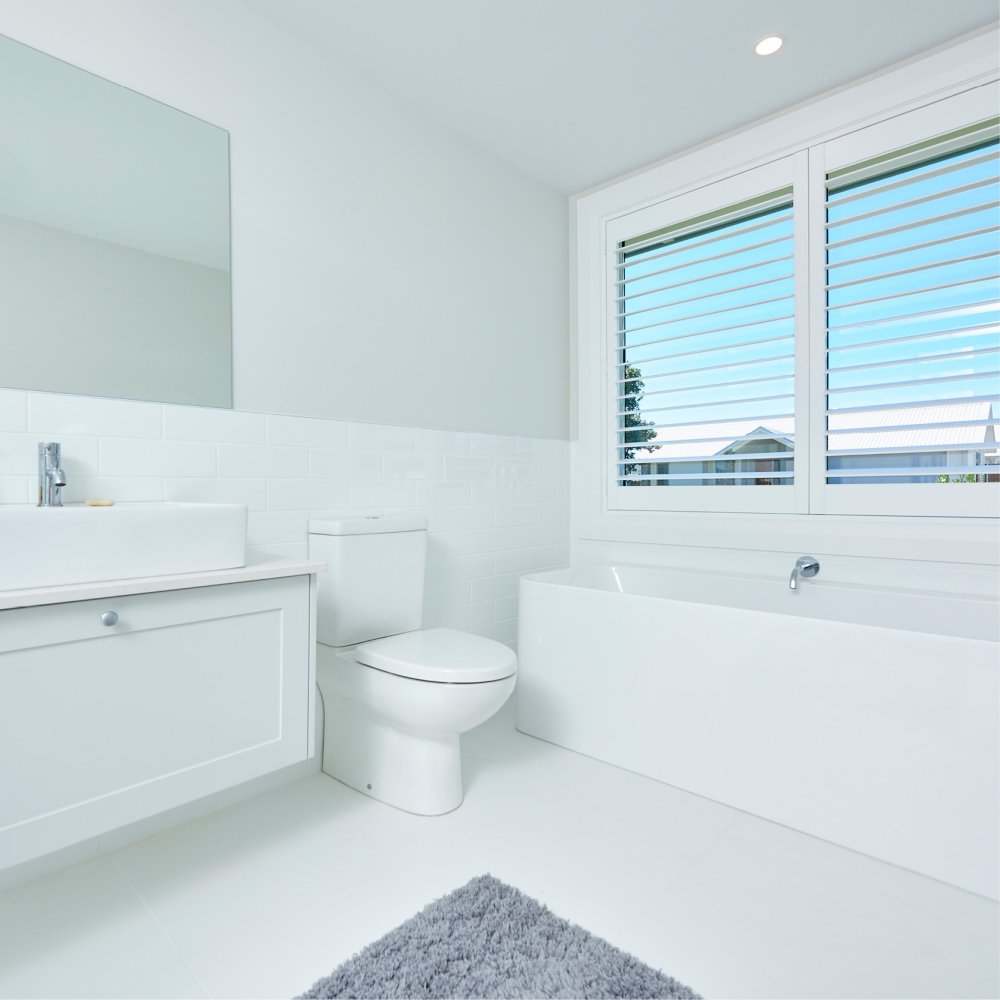 White plantation shutters on a bathroom window above a white tub and vanity.