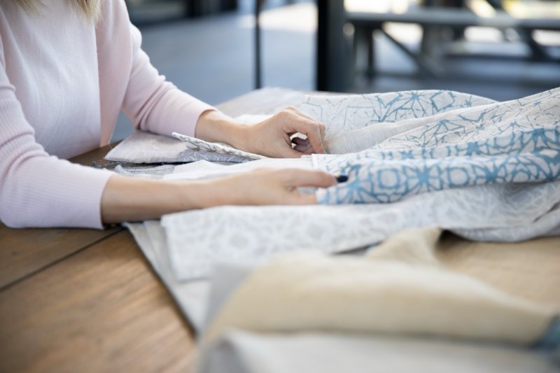 Hands examining cream and blue patterned fabric samples on a wooden table.