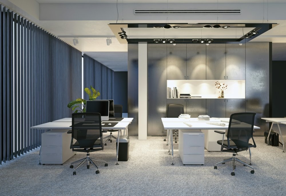 Grey vertical blinds along a modern office wall with white desks and black chairs.