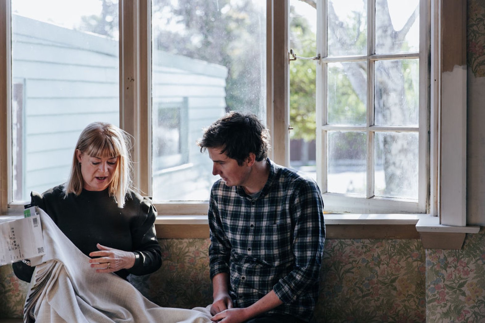 A consultant and customer reviewing fabric samples at a window with brown timber shutters.