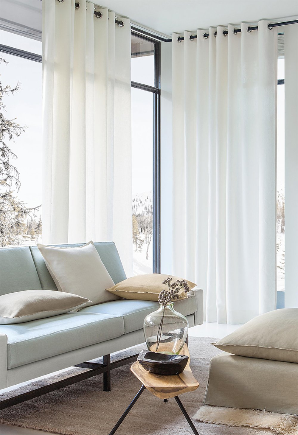 Floor-to-ceiling cream eyelet curtains in a living room with a pale blue sofa and snowy view.