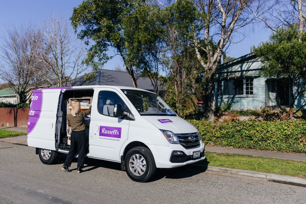 A Russells consultant loading sample books into a branded van on a suburban street for an in-home visit.