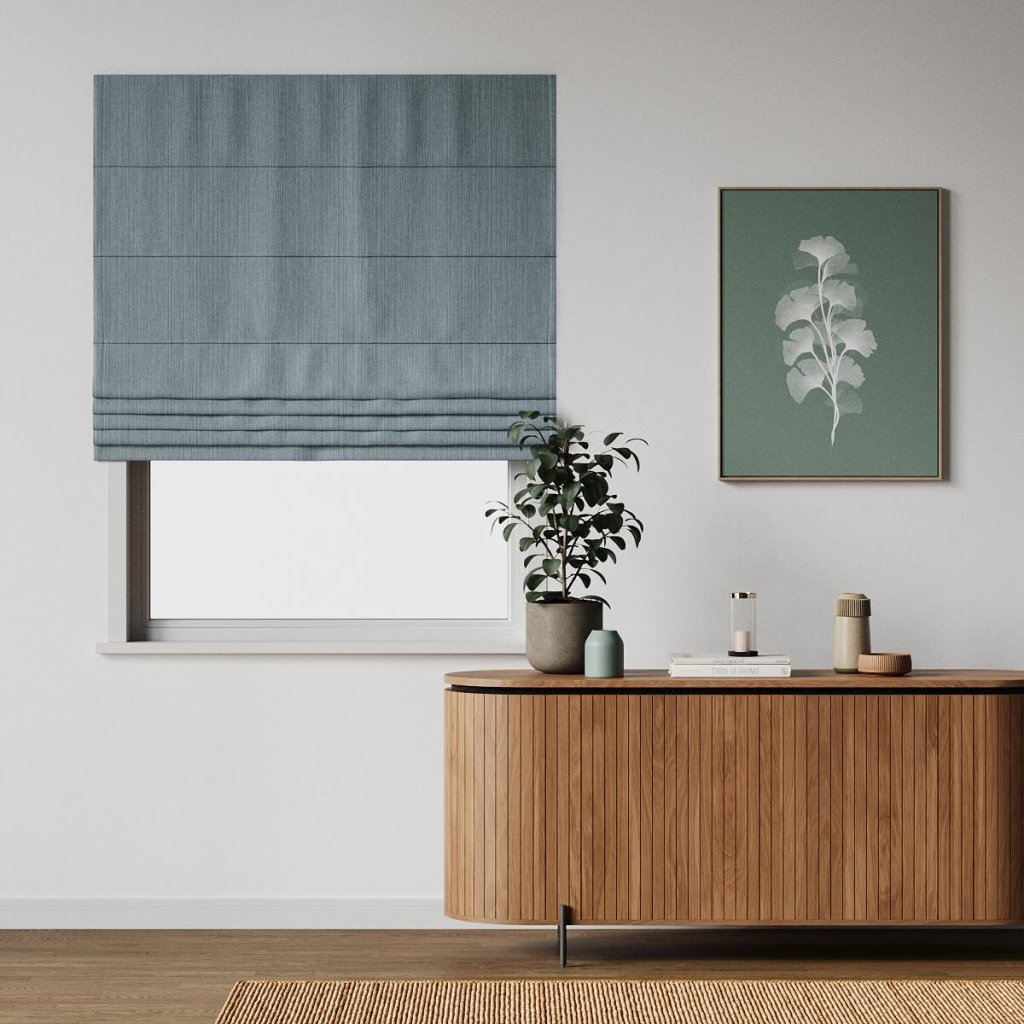 Blue-grey roman blind over a window beside a wooden sideboard with a plant.