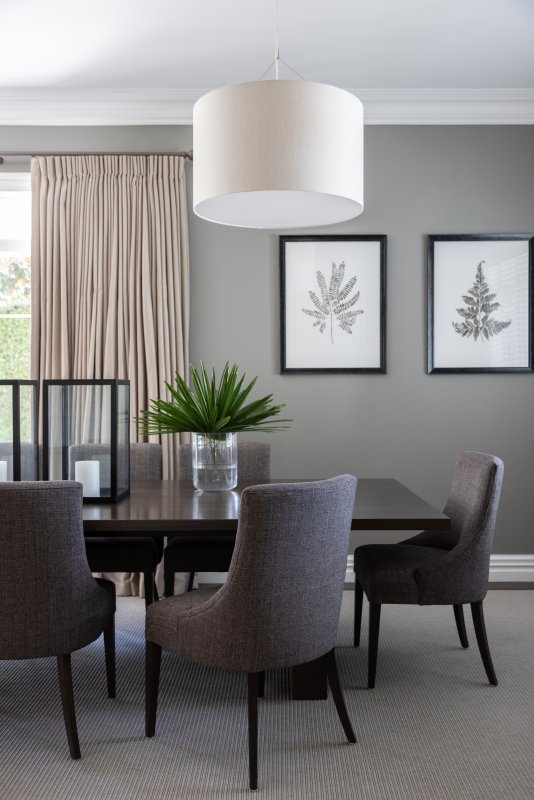Neutral pleated curtains beside a round pendant light in a grey dining room.