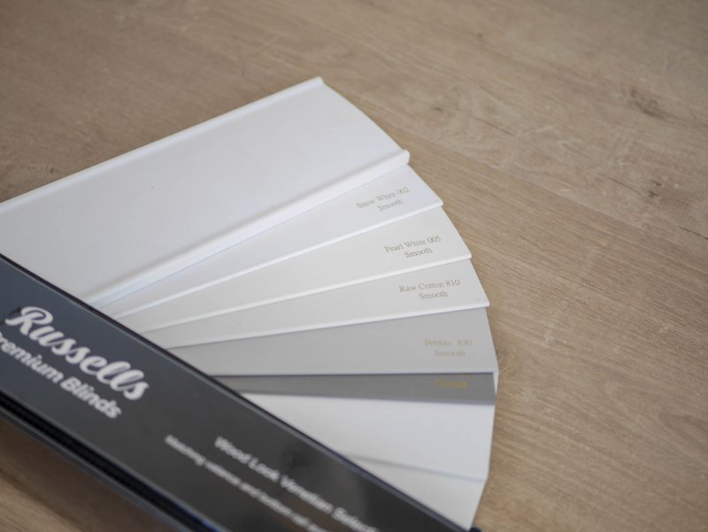 A fan of Russells premium blind fabric swatches in white, cream and beige.