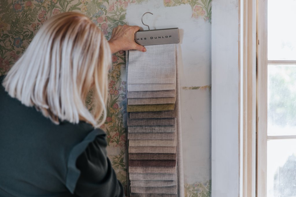 A consultant reviewing fabric swatches against a floral wallpapered wall during a consultation.