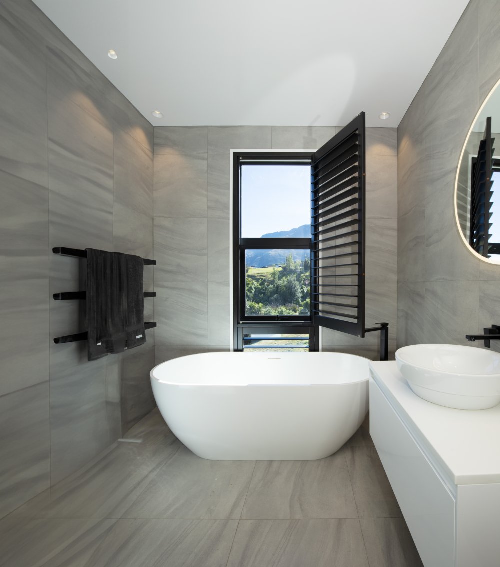 Black timber shutters on a bathroom door with a landscape view and a white bathtub.