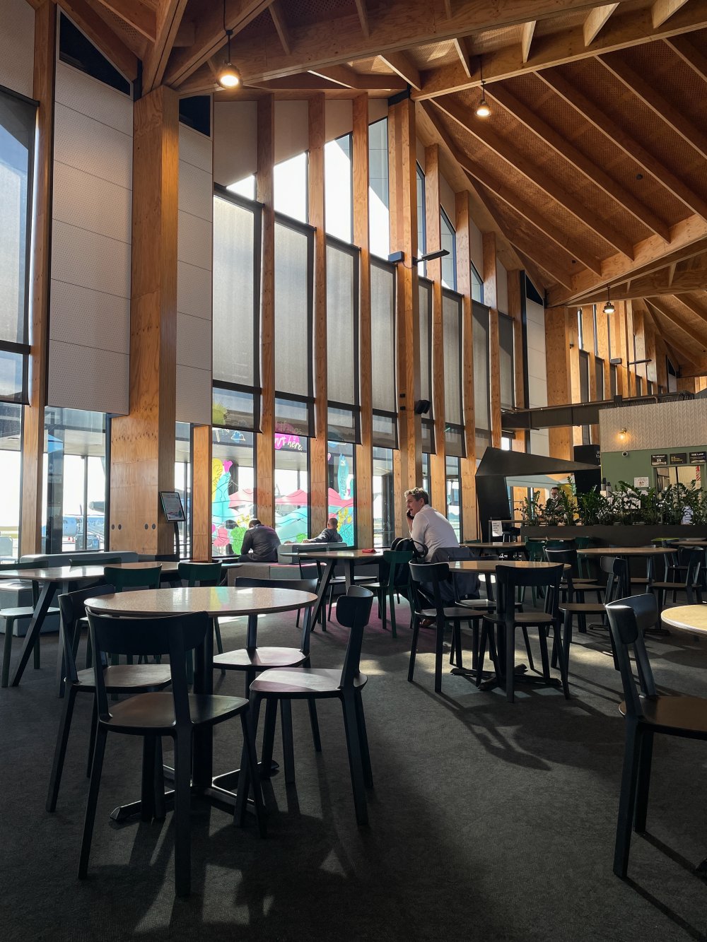 Diners at tables in a timber-beamed hospitality space with full-height windows and drapes.