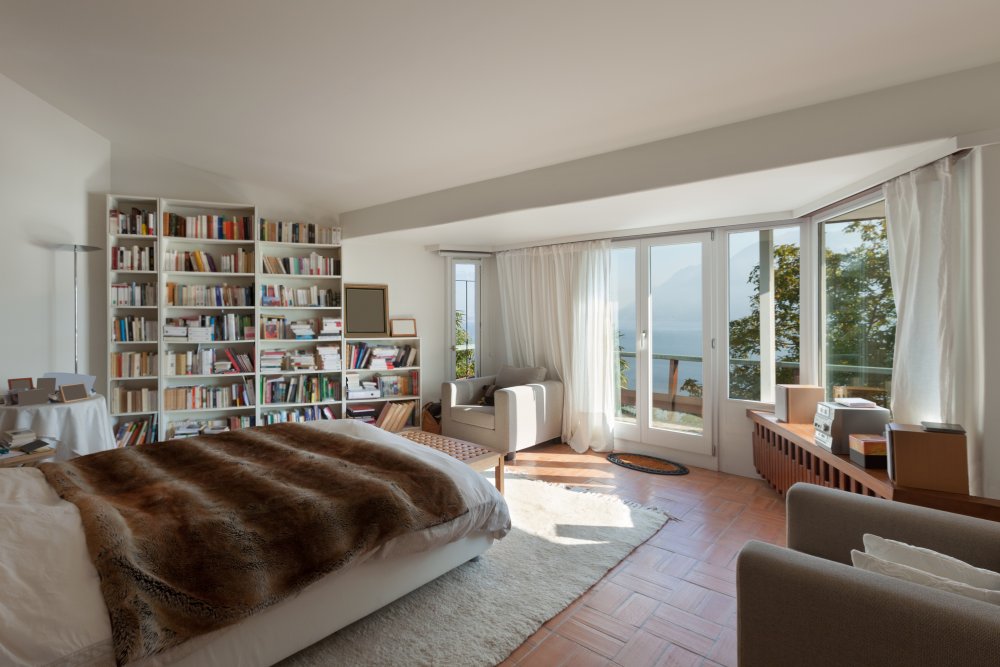 Cream floor-to-ceiling sheers on large windows in a bright bedroom with an ocean view.